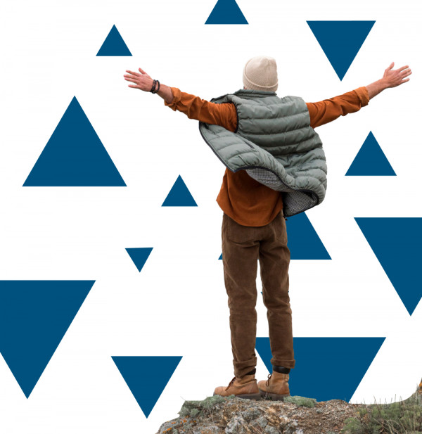 Oseba stoji na skali z razprtimi rokami v zimskih oblačilih obrnjena stran od kamere pred belim ozadjem z modrimi trikotniki kar simbolizira svobodo odprtost in povezanost z naravo