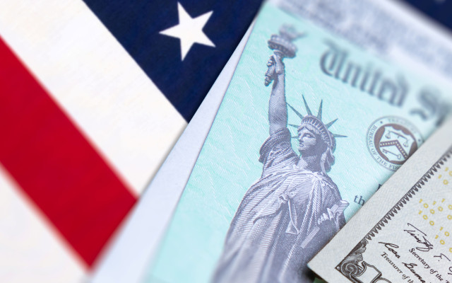 Ameriška zastava in državniški ček z motivom kipa svobode ležita poleg dolarjevega bankovca v simbolični predstavitvi ameriških financ