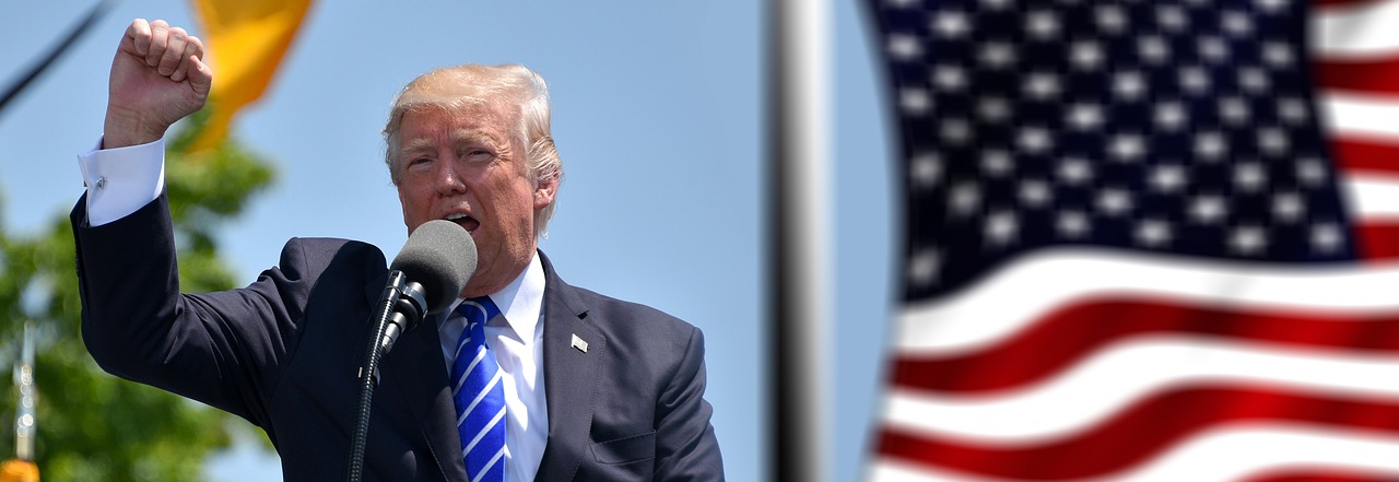 Donald Trump govori v mikrofon in dviguje pest pred ameriško zastavo