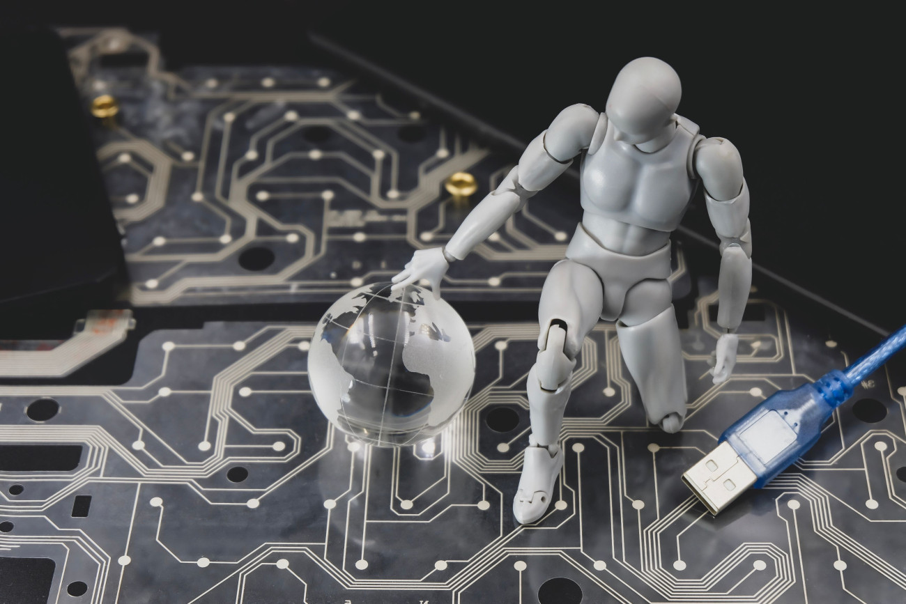 Srebrna robotska figura na vezju kleči ob prosojni krogli z zemljevidom sveta poleg modrega USB kabla