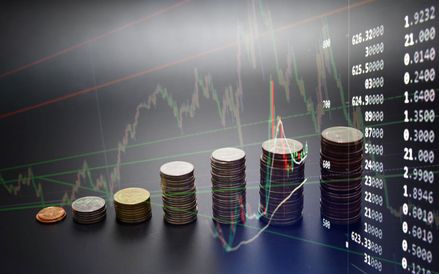 Kupčki kovancev so razporejeni po velikosti pred ozadjem z borznimi grafikoni in številkami