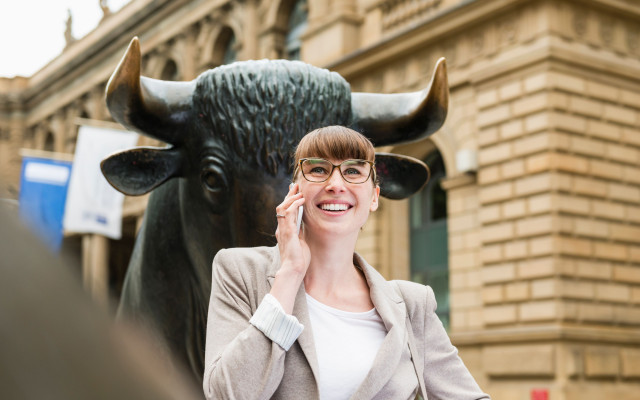 Portret poslovne zenske ki telefonira pred frankrurtsko borzo z ozadjem skulpture bika