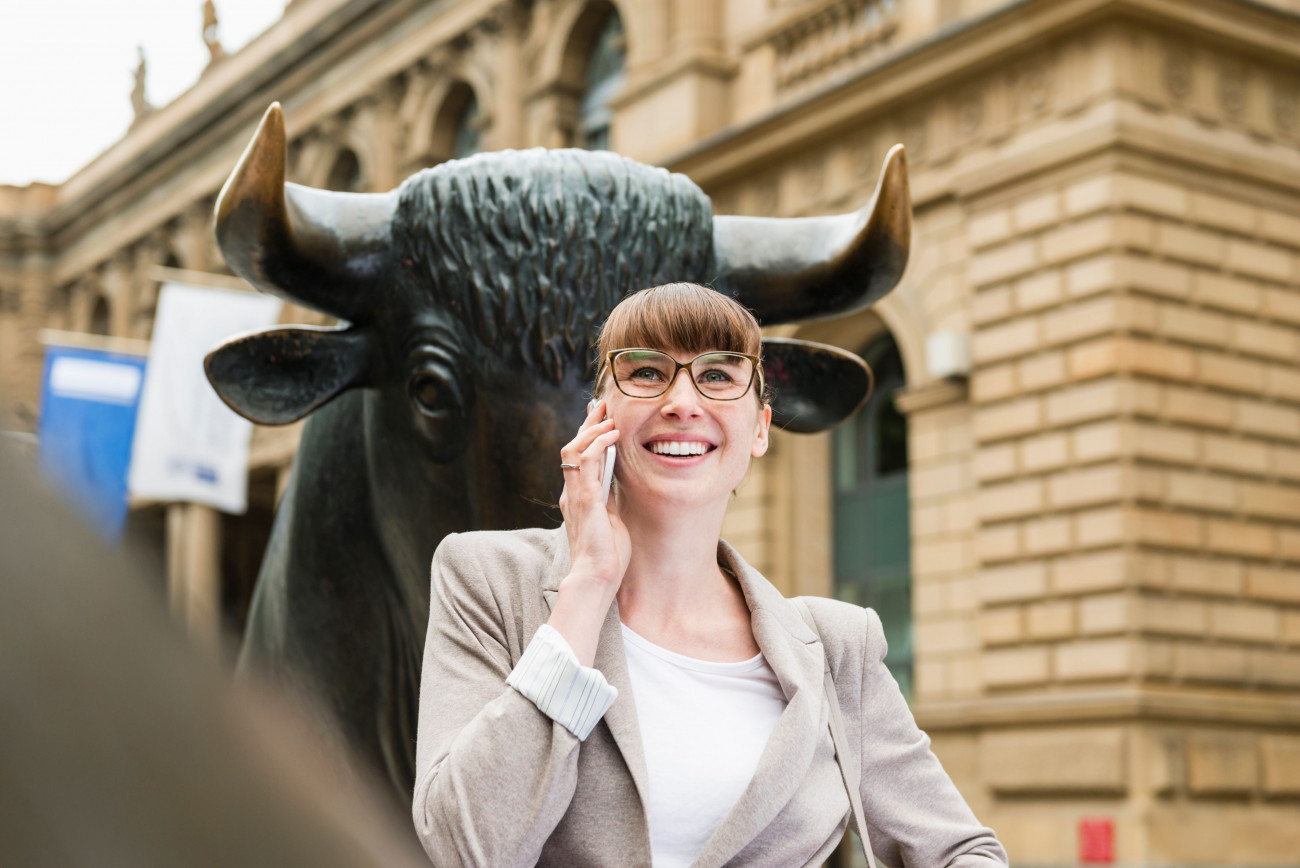 Portret poslovne zenske ki telefonira pred frankrurtsko borzo z ozadjem skulpture bika