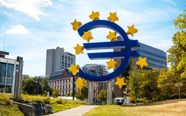 Velik moder simbol evra obdan z rumenimi zvezdami stoji na zelenici pred mestom Frankfurt