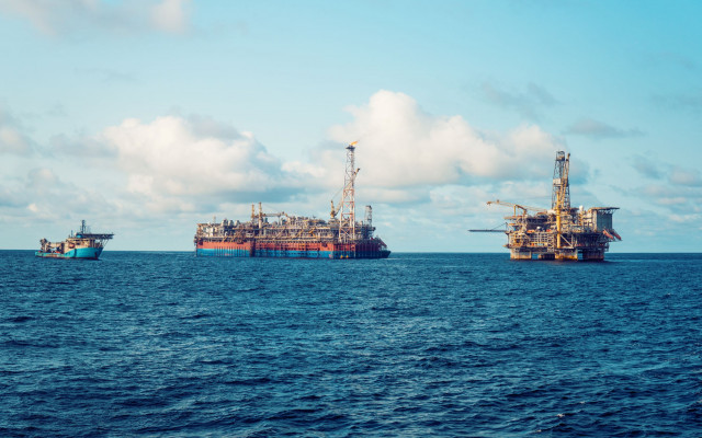 Na odprtem morju sta dve veliki naftni ploščadi in ladja pod oblačnim nebom