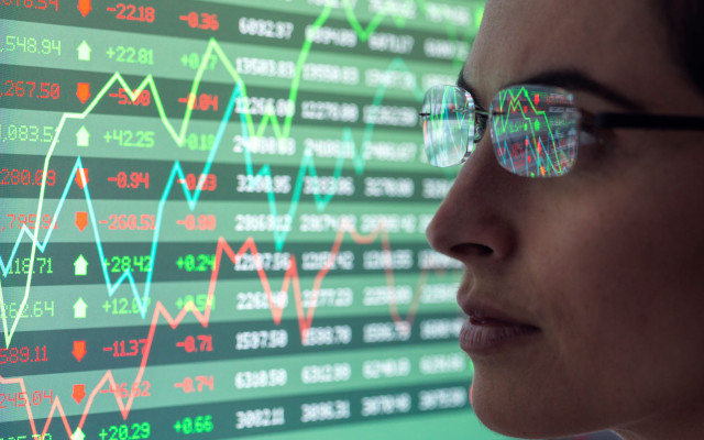 Ženska z očali od blizu opazuje zaslon z grafi in številkami finančnega trga