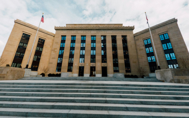 Pred zgradbo ameriške centralne banke Federal Reserve v Washingtonu vidimo široke kamnite stopnice pod oblačnim nebom z ameriškima zastavama na obeh straneh 