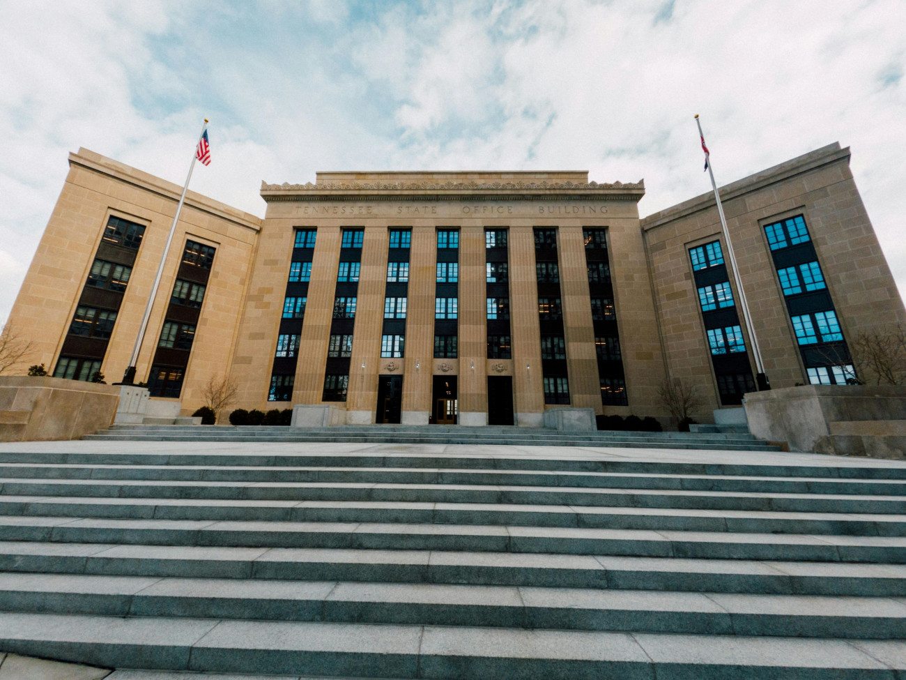 Pred zgradbo ameriške centralne banke Federal Reserve v Washingtonu vidimo široke kamnite stopnice pod oblačnim nebom z ameriškima zastavama na obeh straneh 