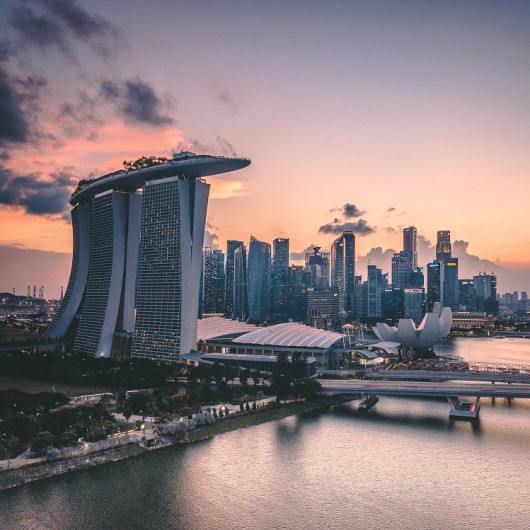 Pogled na sodobno mestno obzorje Singapurja z osvetljenimi stolpnicami in znamenito stavbo Marina Bay Sands ob sončnem zahodu nad zalivom