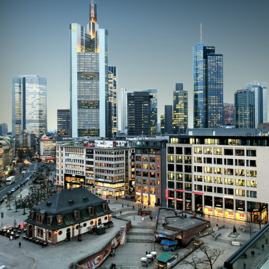 Mestno središče Frankfurta z mešanico modernih stolpnic in zgodovinske arhitekture pod večernim nebom s prižganimi lučmi v izložbah