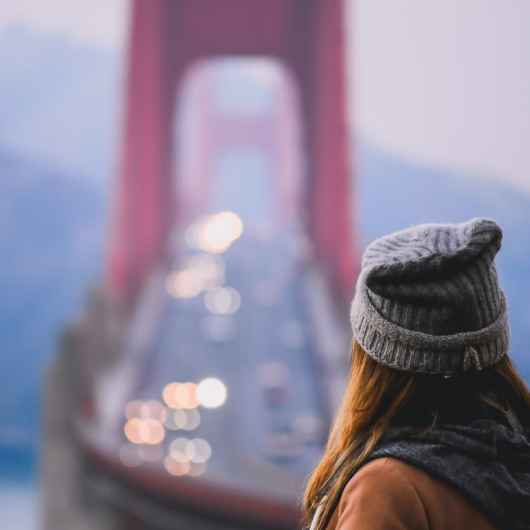 Oseba z volneno kapo zre proti  Golden Gate mostu ob prometni cesti 
