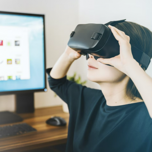 Otrok z virtualnimi očali sedi pred računalniškim zaslonom in raziskuje navidezno resničnost v pisarniškem okolju