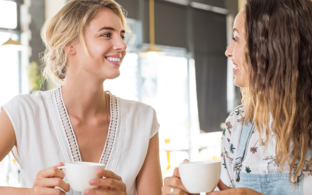 Dve mladi ženski v svetlem prostoru ob kavi sproščeno klepetata in se smehljata