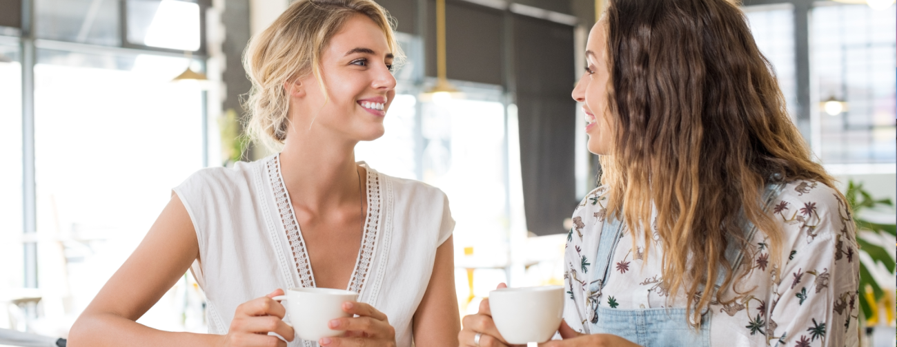 Dve mladi ženski v svetlem prostoru ob kavi sproščeno klepetata in se smehljata