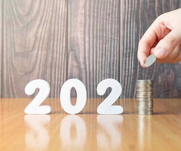 Roka dodaja kovanec na kupček ki predstavlja številko ena in skupaj z belimi številkami tvori letnico 2021 kar simbolizira finančne cilje ali varčevanje v novem letu