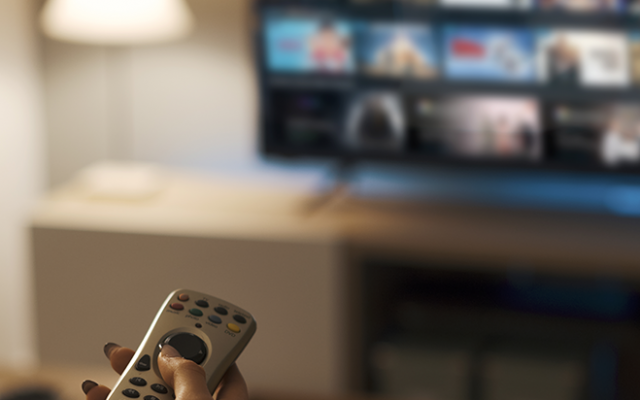 Na sliki je oseba s daljincem v roki pred televizorjem z izbranim programom za gledanje