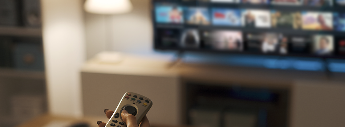 Na sliki je oseba s daljincem v roki pred televizorjem z izbranim programom za gledanje