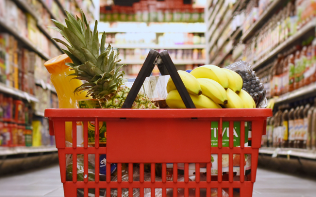 Na sliki je rdeča nakupovalna košara polna živil v trgovini med policami.