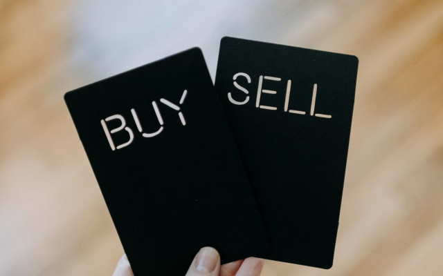 Roka drži dve črni kartici z izrezanima napisoma buy in sell kar simbolizira odločanje med nakupom in prodajo