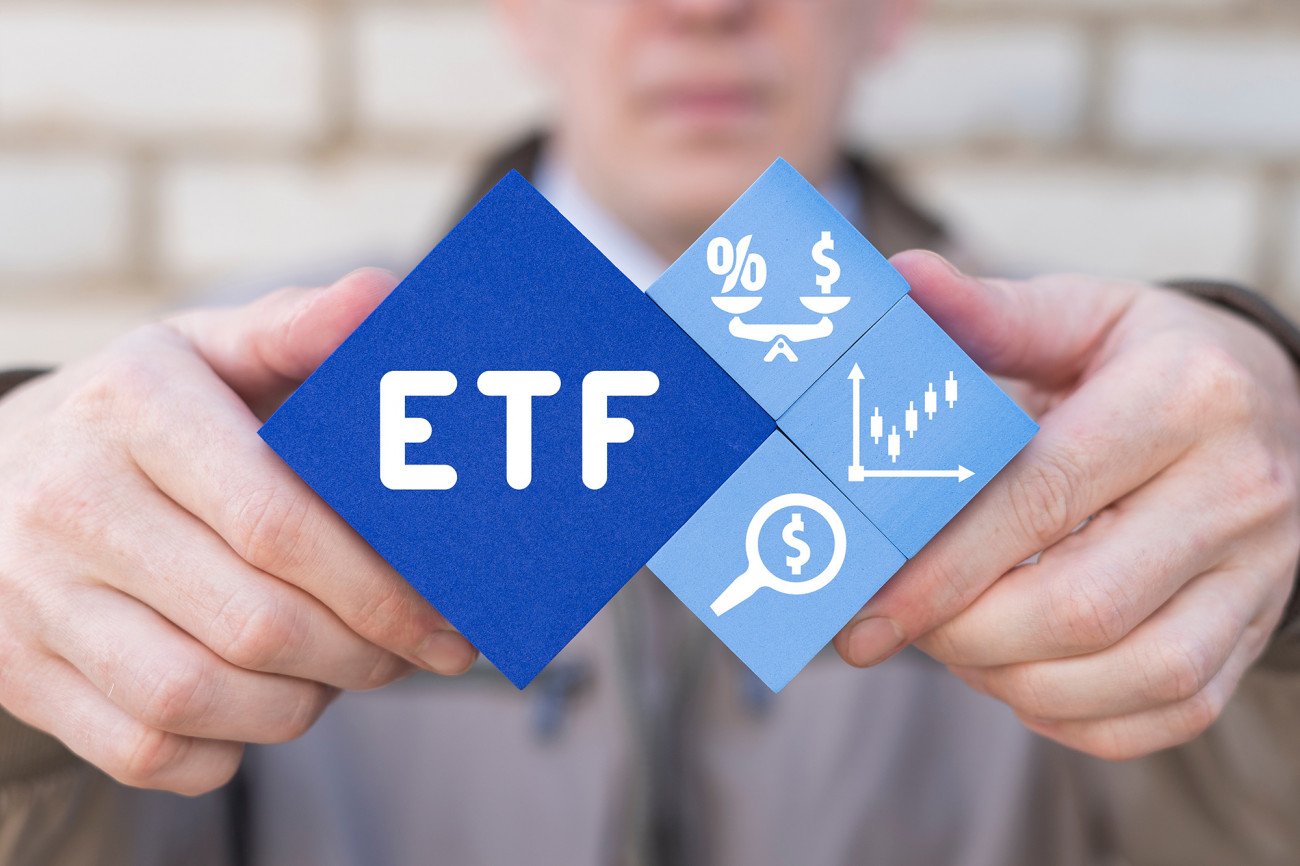 Oseba drži modre kocke s napisom ETF in ikonami, ki simbolizirajo donose, raziskovanje in rast naložb.