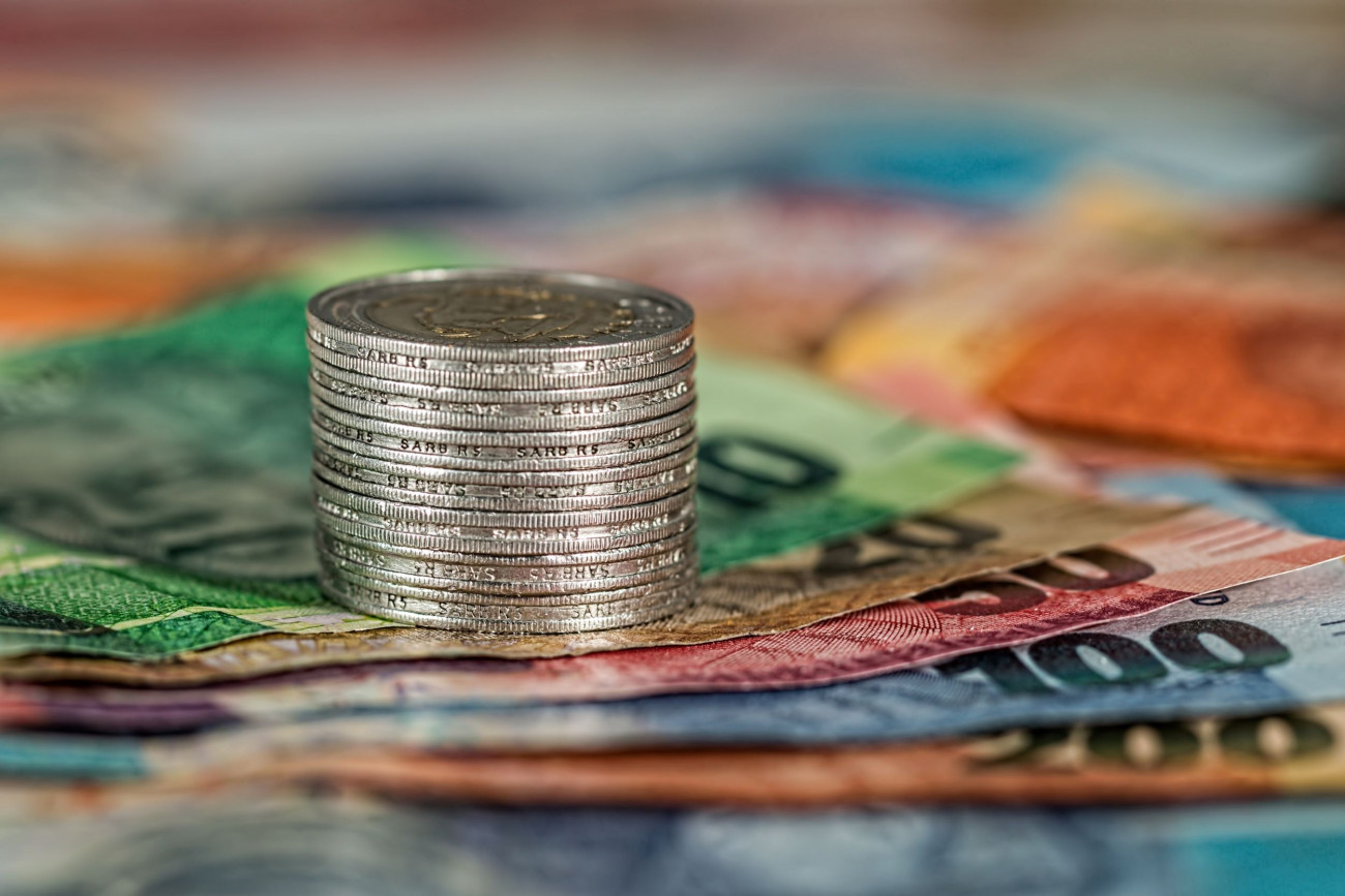 Na sliki je kup kovancev ki stoji na kupu barvitih bankovcev kar simbolizira bogastvo finance ali varčevanje