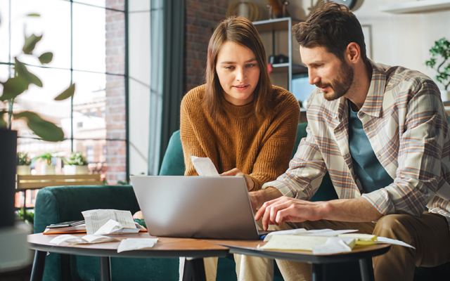 Par v tridesetih sedi na kavču in gleda v prenosni računalnik na klubski mizici