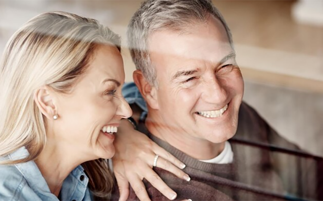 Nasmejan starejši par se objema in gleda skozi okno v svetlem prostoru