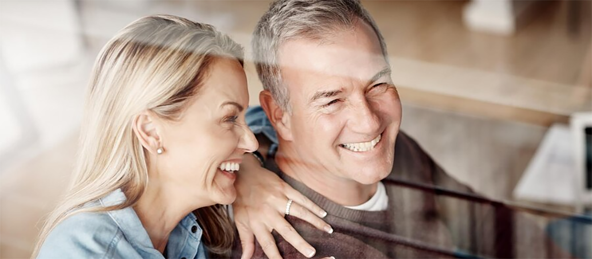 Nasmejan starejši par se objema in gleda skozi okno v svetlem prostoru