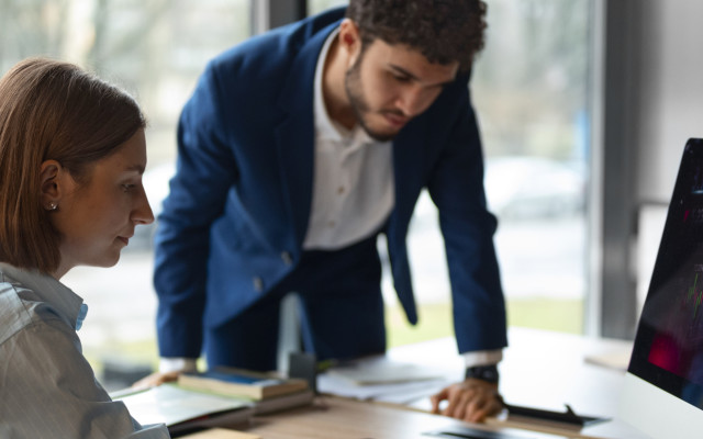 Slika prikazuje finančna strokovnjaka, žensko in moškega, ki gledata na računalniški zaslon s finančno analizo.