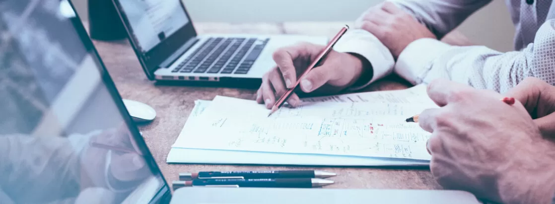 Slika prikazuje roko osebe, ki s svinčnikom kaže na podatek, zapisan na listu papirja