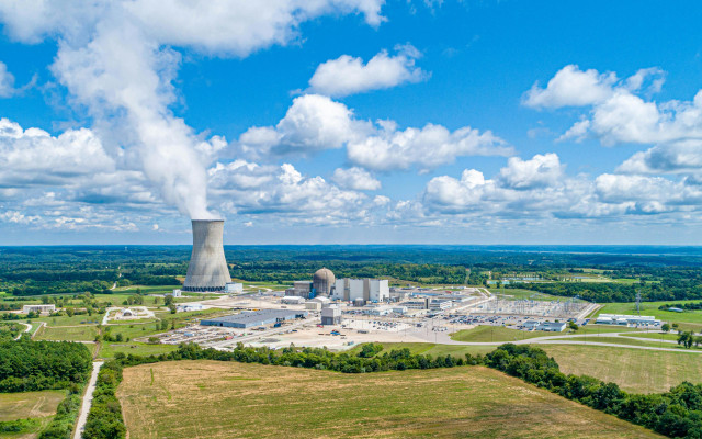 Jedrska elektrarna s hladilnim stolpom, iz katerega se dviga para, v odprti pokrajini pod modrim nebom z oblaki