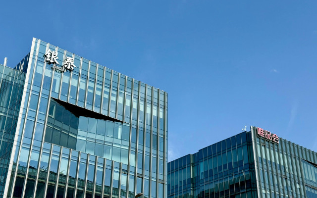 Sodobni stekleni poslovni stavbi z napisoma v kitajskih znakih pod jasnim modrim nebom.