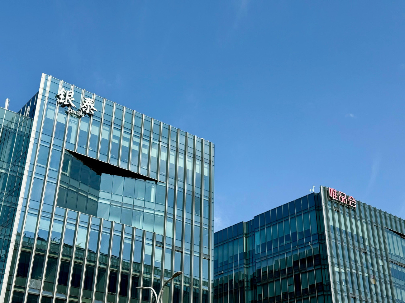 Sodobni stekleni poslovni stavbi z napisoma v kitajskih znakih pod jasnim modrim nebom.