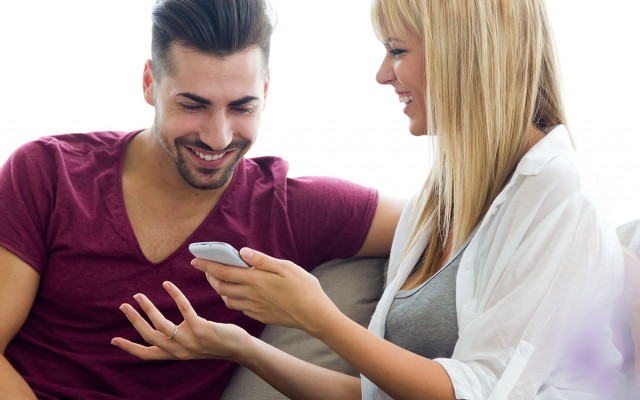 Nasmejan par sedi na kavču in skupaj gleda telefon med sproščenim pogovorom