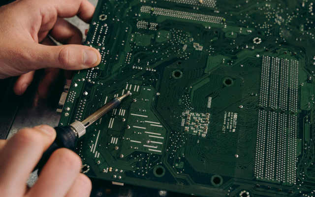 Oseba s spajkalnikom popravlja ali lota vezje na zelenem tiskanem vezju