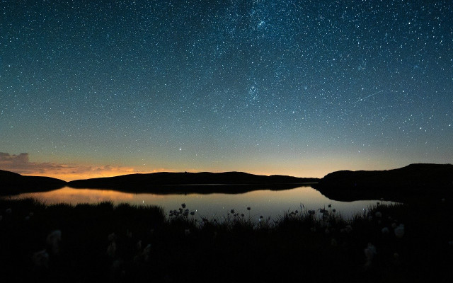 Jezero obdano s hribi odseva zvezdnato nebo ob večerni svetlobi na obzorju