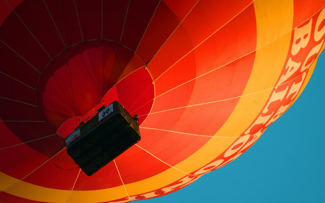 Pogled od spodaj na pisan rdeče rumen toplozračni balon z visečo košaro, ki lebdi na jasnem nebu