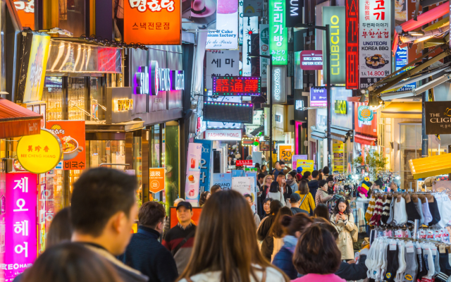 Živahna mestna ulica v Južni Koreji z množico ljudi in svetlečimi neonskimi napisi trgovin.