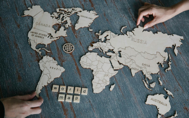 Lesena sestavljanka svetovnega zemljevida na mizi, z rokama, ki premikata del zemljevida, in napisom »world map«