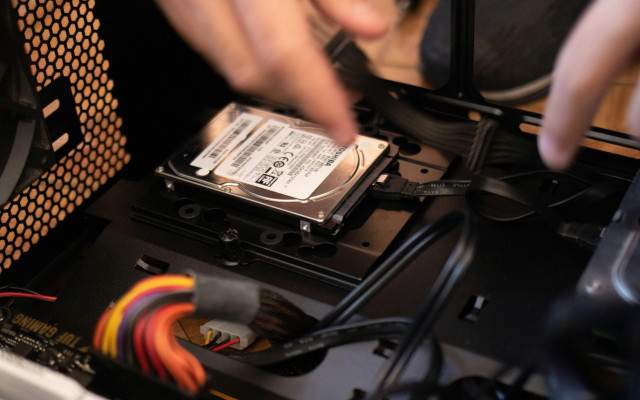 Oseba v računalniškem ohišju priključuje ali namešča trdi disk, obdana s kabli in komponentami