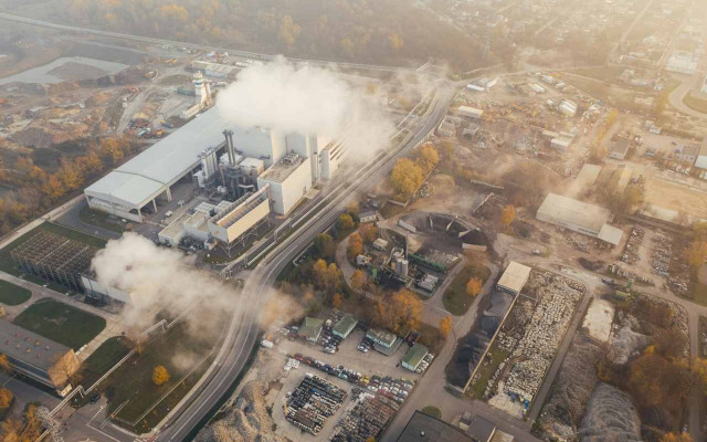 Zračni posnetek industrijskega obrata iz katerega se kadi obdanega z gradbišči in skladišči