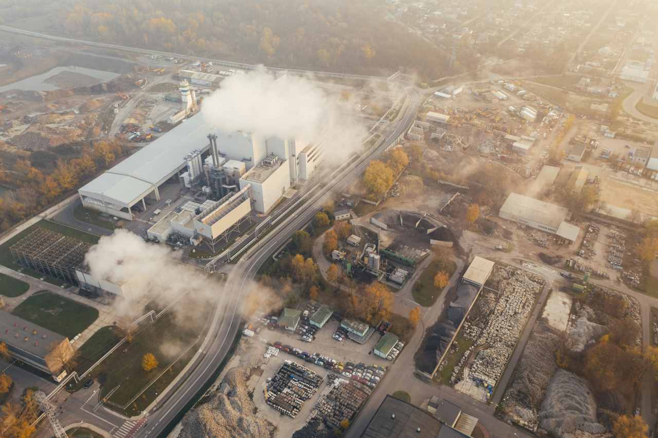 Zračni posnetek industrijskega obrata iz katerega se kadi obdanega z gradbišči in skladišči