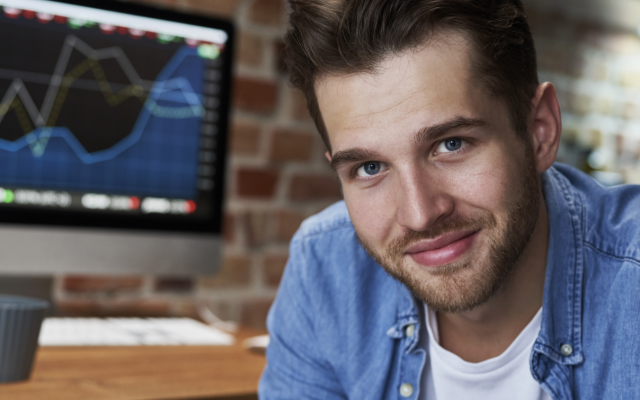 Slika prikazuje finančnega strokovnjaka ob pisalni mizi, na kateri sta računalniška monitorja s prikazom gibanja vrednosti finančnih instrumentov.