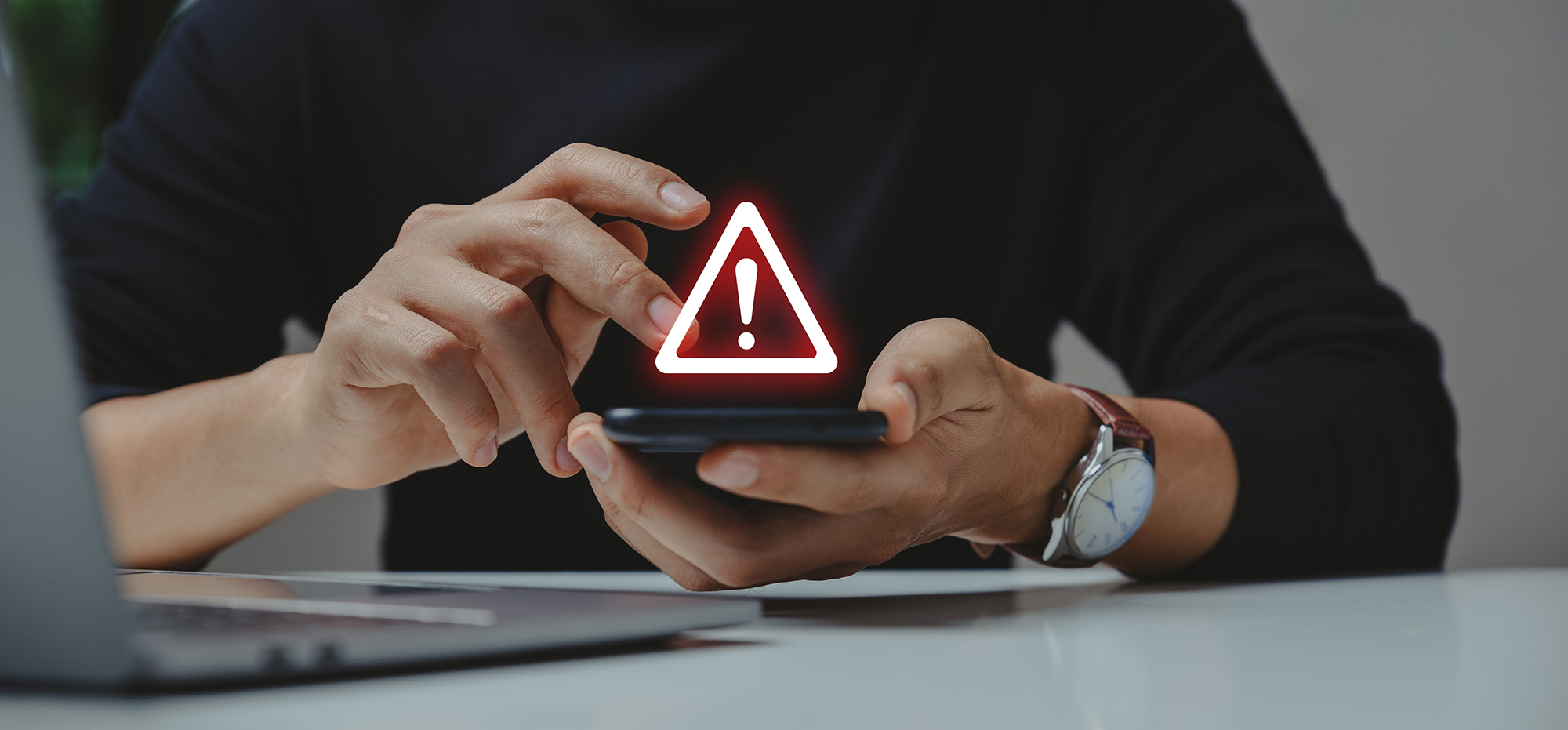 Oseba drži pametni telefon z opozorilnim znakom z rdečim klicajem na zaslonu kar nakazuje na varnostno ali sistemsko težavo