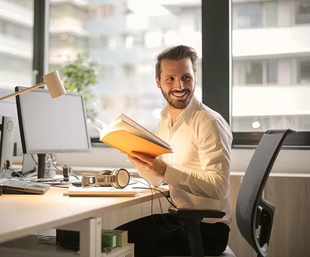 Slika finančnega strokovnjaka za pisalno mizo, na mizi je računalniški zaslon. Strokovnjak gleda vstran, v roki drži zvezek.