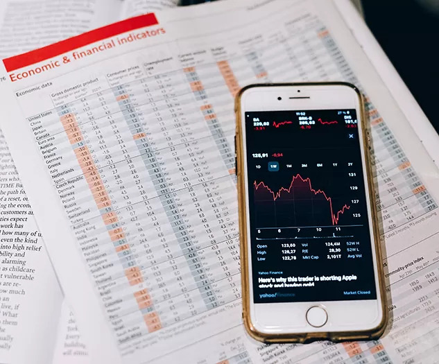 Slika prikazuje mobilni telefon z odprto finančno aplikacijo, v kateri se izrisuje grafikon gibanja vrednosti naložbe