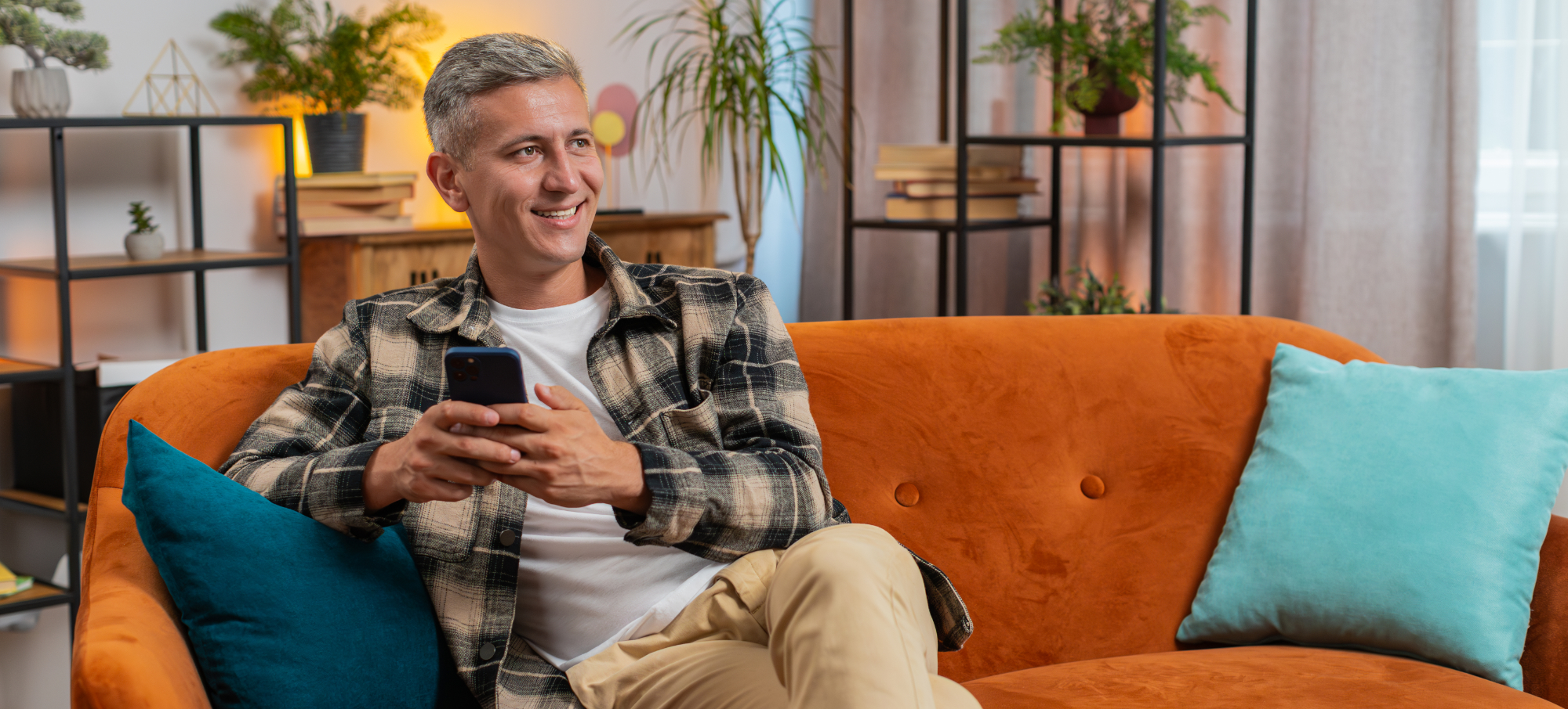 Slika moškega na kavču, ki ima v rokah mobilni telefon