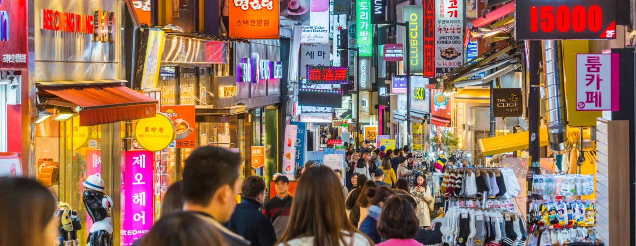Živahna mestna ulica v Juzni Koreji z množico ljudi in svetlečimi neonskimi napisi trgovin
