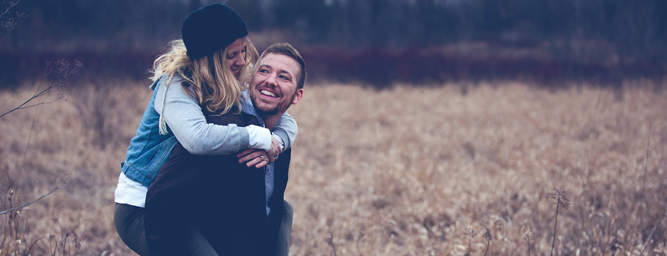 Slika mladega para sredi polja, moški nosi žensko na hrbtu
