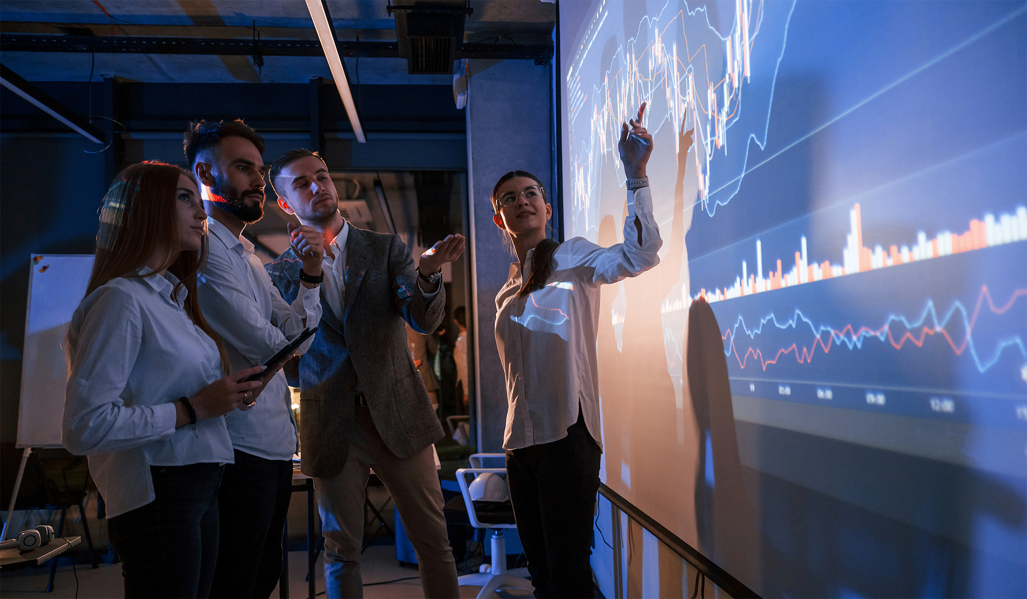 Skupina finančnih analitikov analizira grafe in trende na veliki digitalni projekciji v sodobni pisarni
